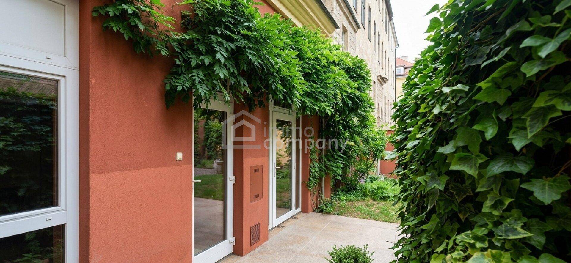 Eine kleine Terrasse mit Zugang zum Garten, umgeben von grünen Pflanzen und Efeu an der Fassade.