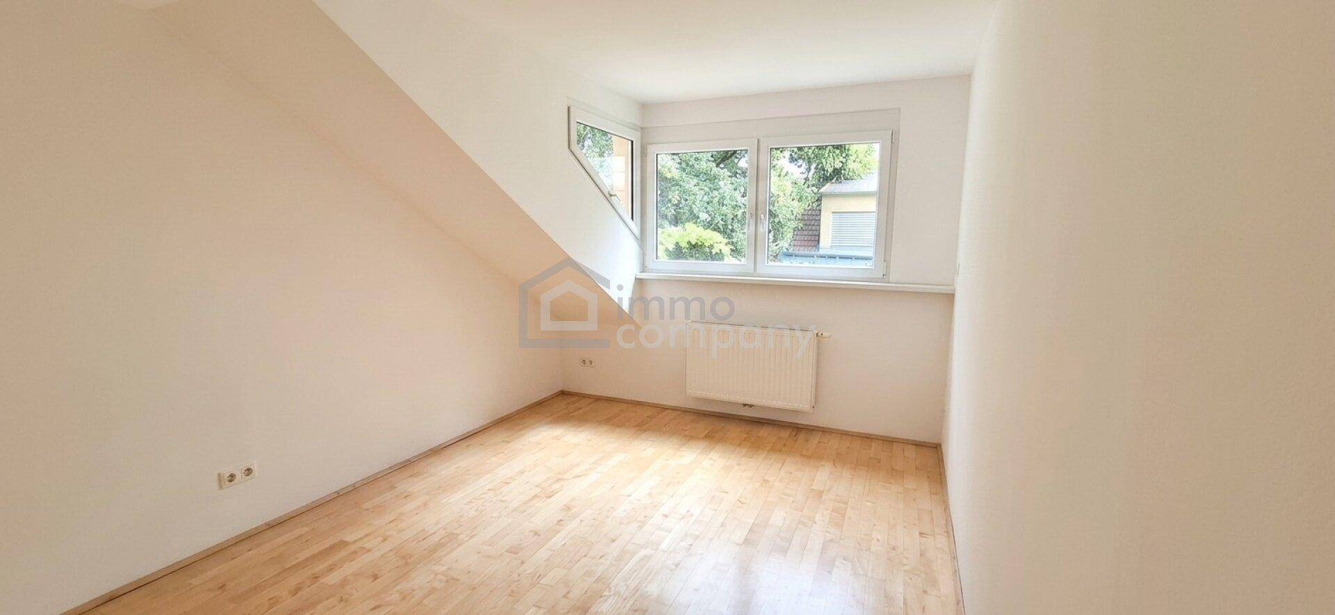 Helles Schlafzimmer im Dachgeschoss mit Holzboden, Dachschräge und großem Fenster mit Blick ins Grüne.