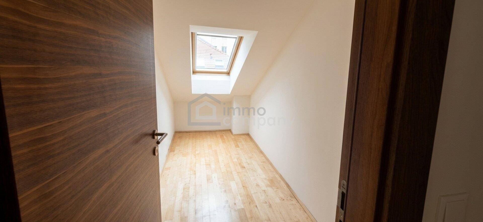 Leeres Zimmer im Dachgeschoss mit Holzboden, Dachfenster und schrägen Wänden, ideal als Schlafzimmer.