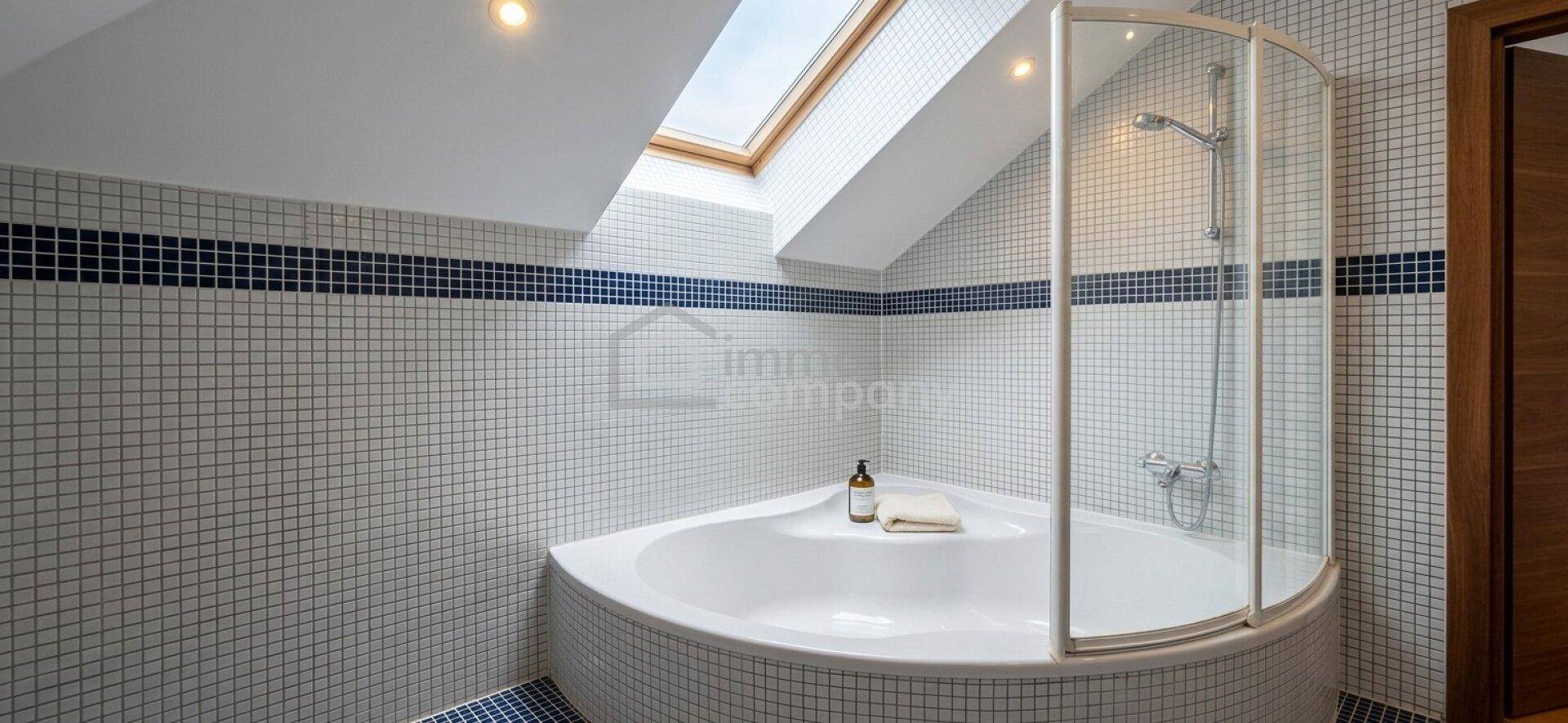 Badezimmer im Dachgeschoss mit Eckbadewanne, Duschkabine und Dachfenster, gefliest mit Mosaikfliesen.