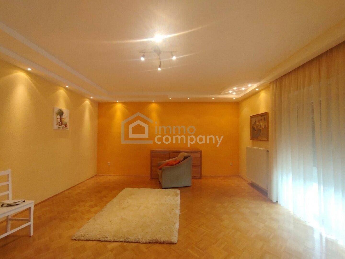 Geräumiges Wohnzimmer mit gelben Wänden, Parkettboden und großem Fenster für viel Tageslicht.