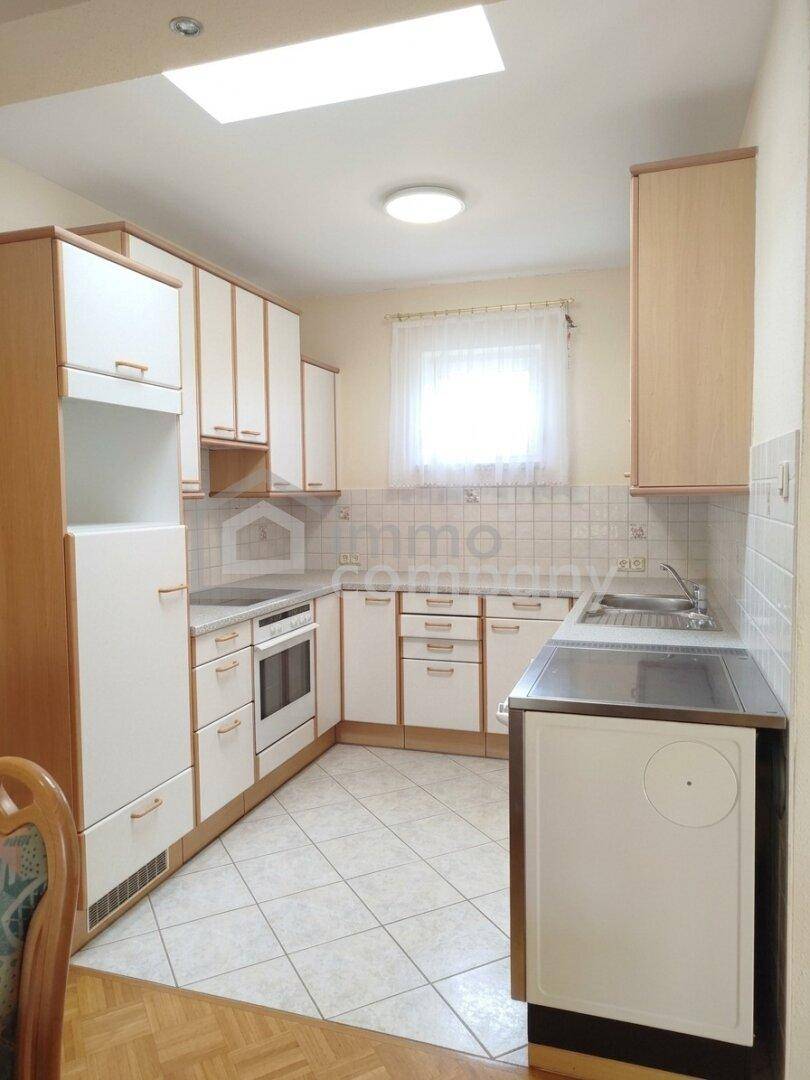 Funktionale Küche mit weißen Schränken, Fliesenboden und Dachfenster für natürliches Licht beim Kochen.