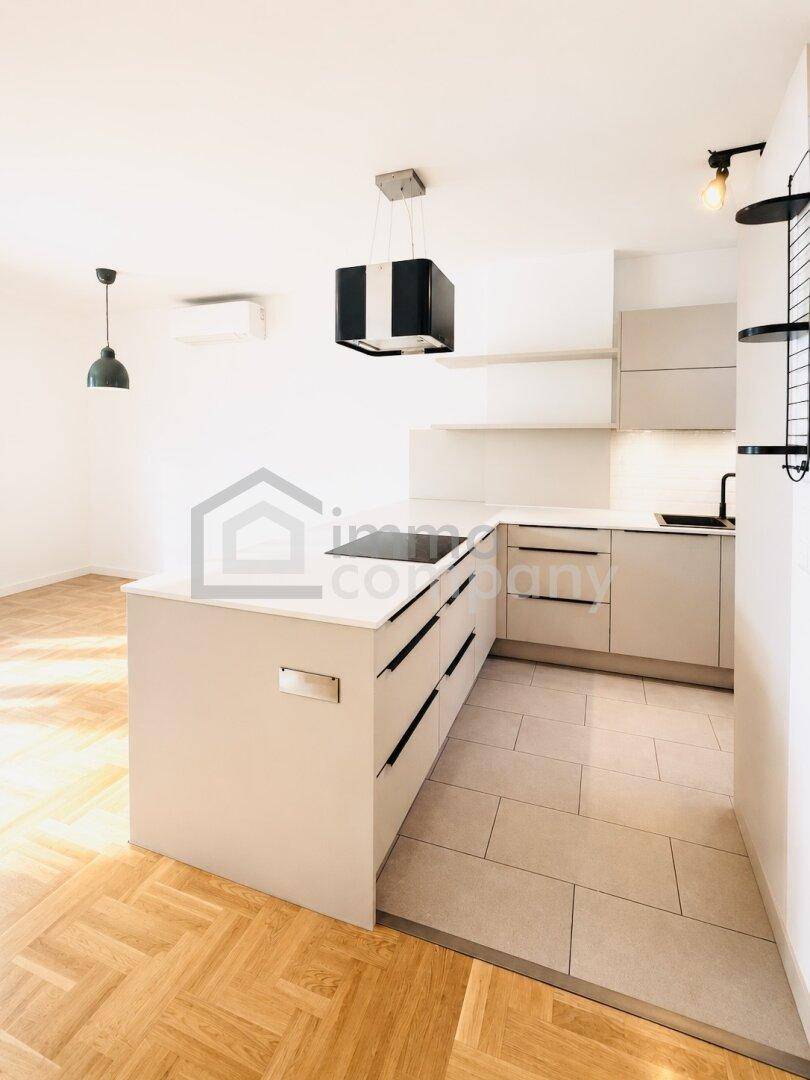 Moderne Küche mit Kücheninsel, Induktionskochfeld und hellem Fischgrätparkett im Wohnbereich.