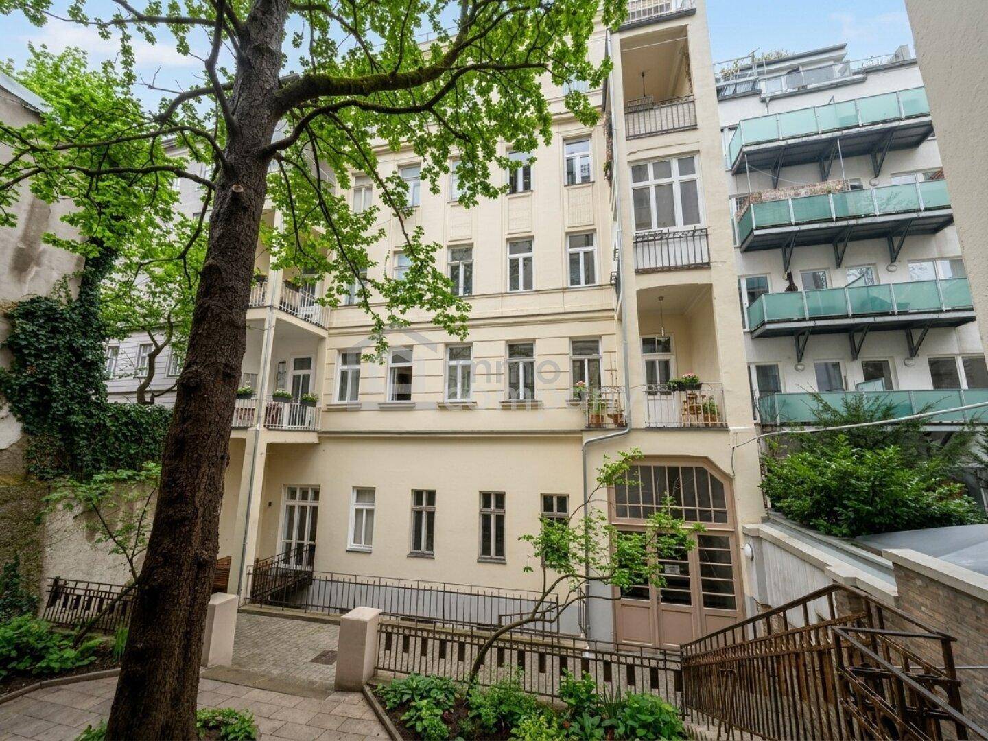 Grüner Innenhof eines Altbaus mit Bäumen, Efeu und Balkonen, der eine ruhige Atmosphäre bietet.