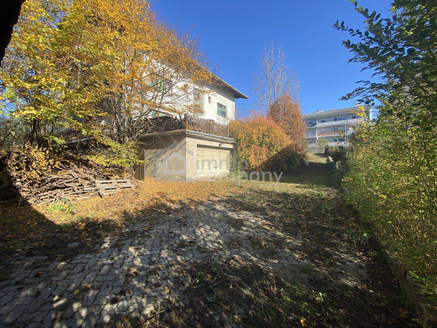 Außenansicht des Anwesens mit gepflasterter Auffahrt, Garage und herbstlichem Garten.