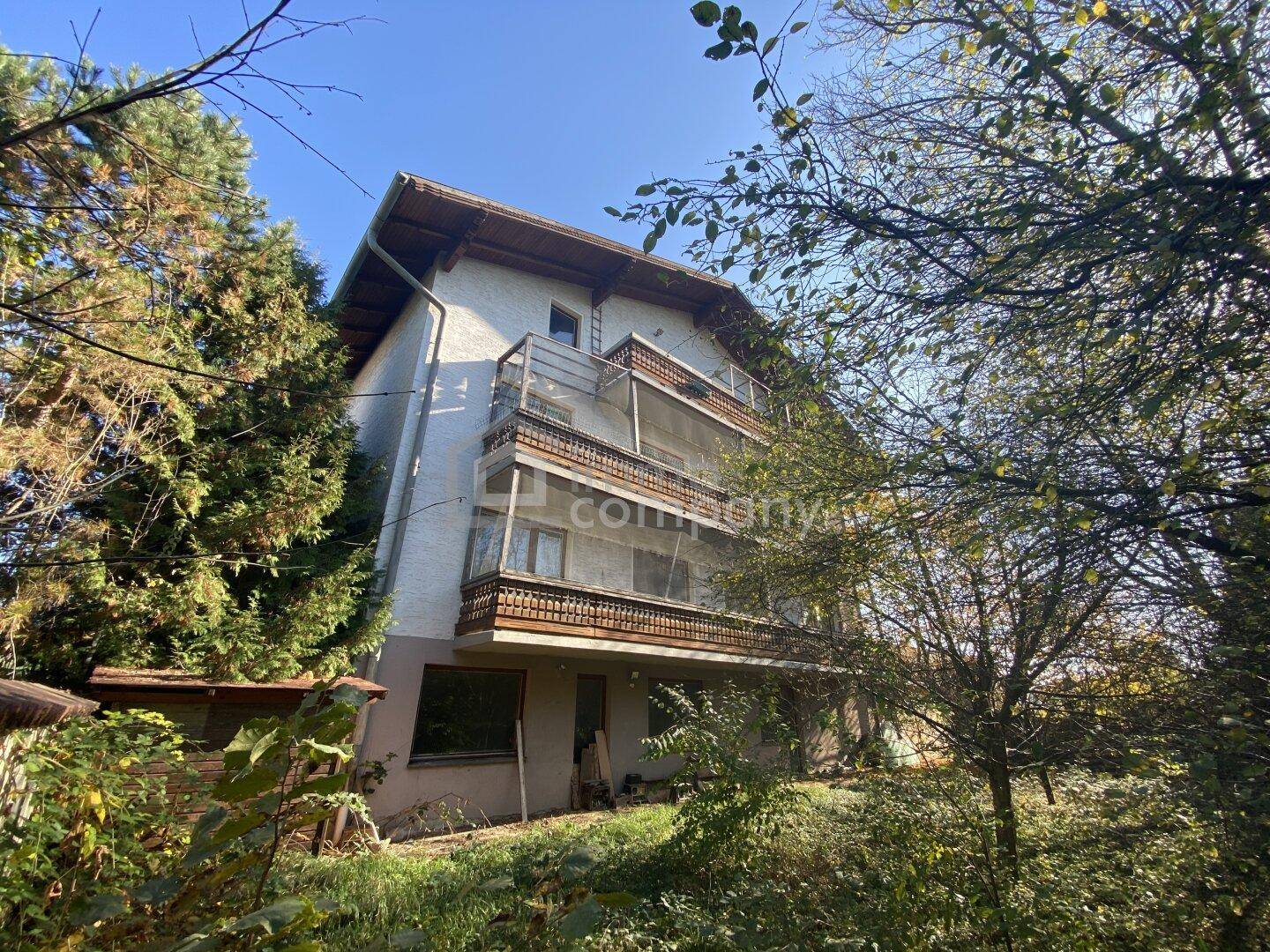 Mehrstöckiges Wohnhaus mit mehreren Balkonen, umgeben von Bäumen und Vegetation.