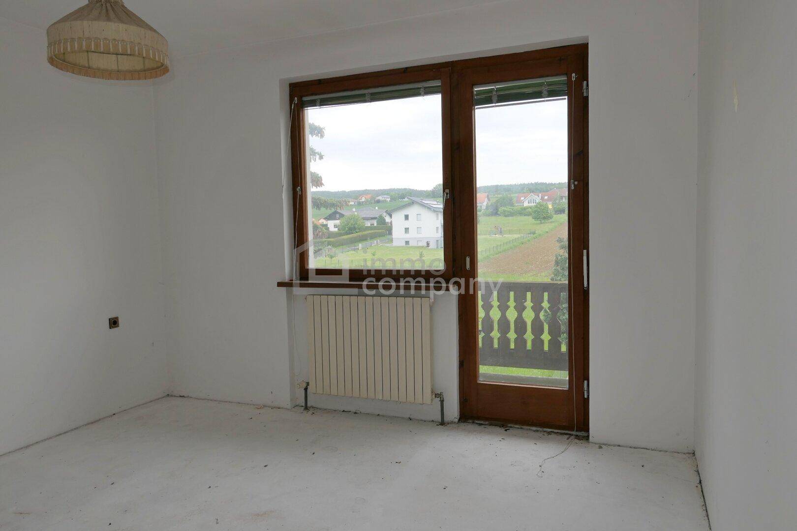 Leeres Zimmer mit Zugang zu einem kleinen Balkon und weitem Blick auf die Landschaft.