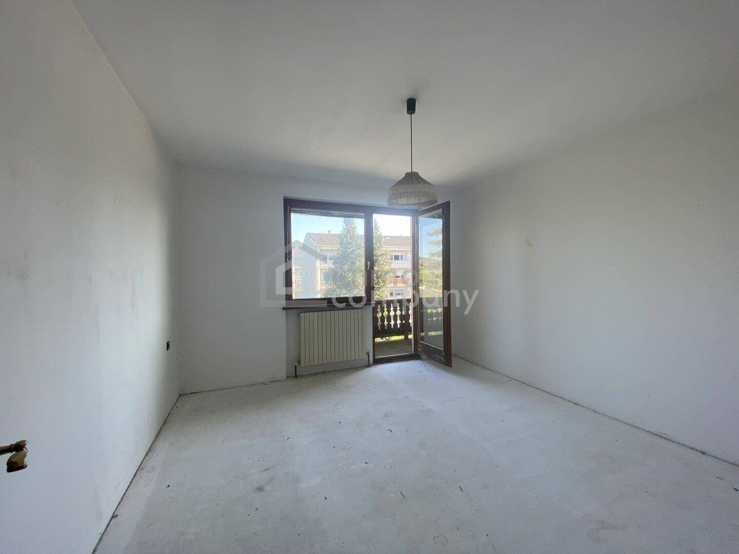 Helles Zimmer mit Balkonzugang und Blick auf die umliegende Bebauung und Bäume.