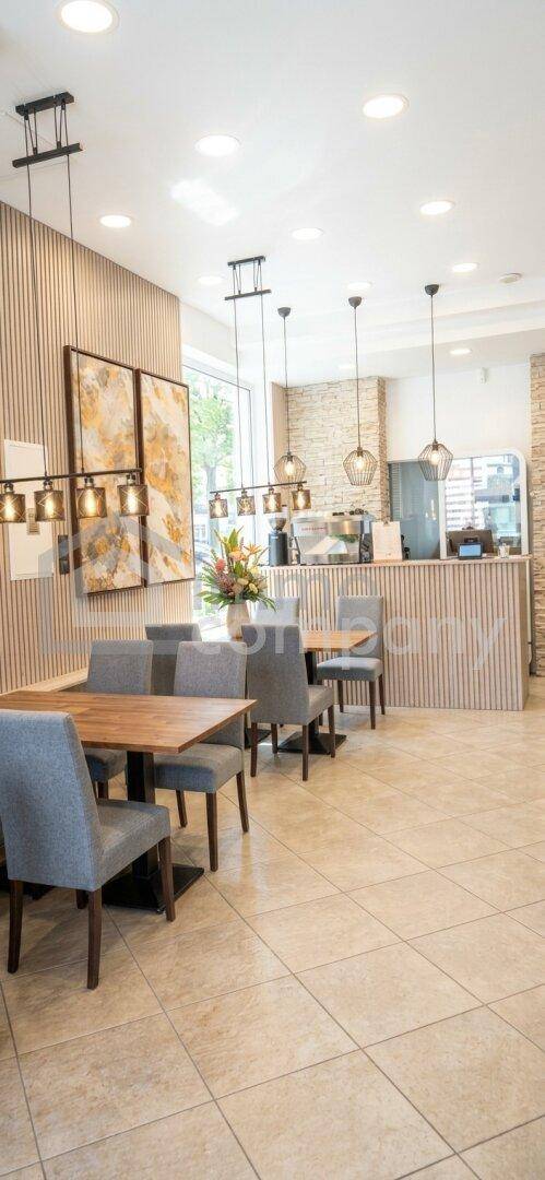 Modernes Restaurant mit Holzakzenten, Fliesenboden und stilvoller Beleuchtung. Es gibt mehrere Tische und eine Theke im Hintergrund.