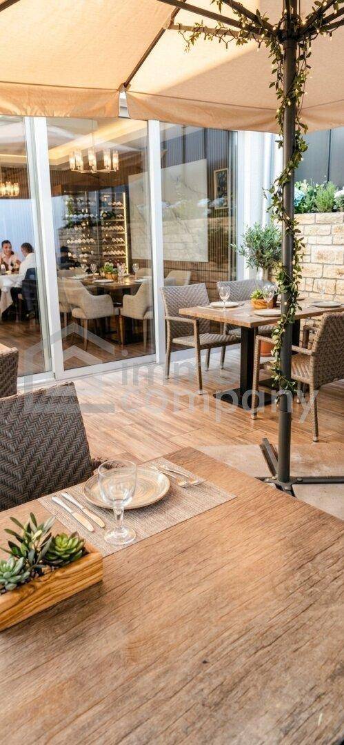 Gemütliche Außenterrasse mit Holztischen, Sonnenschirm und Blick auf den Innenbereich. Ideal für Mahlzeiten im Freien.