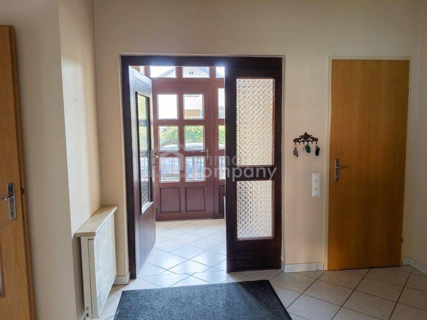 Heller Eingangsbereich mit gefliestem Boden und einer Holztür mit Glaseinsätzen.