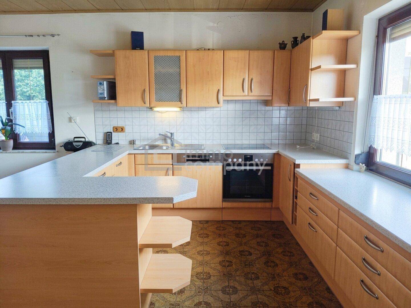 Funktionale Küche mit Holzschränken, Fliesenspiegel und integrierten Geräten sowie Essbereich.