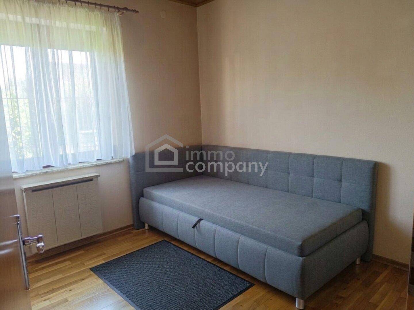 Schlafzimmer mit Holzboden, großem Fenster und einem Schlafsofa, hell und freundlich.