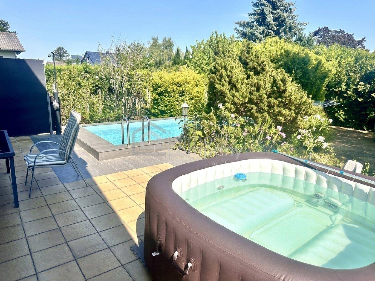 Entspannungsbereich im Freien mit Pool, Whirlpool und Gartenmöbeln, umgeben von einer Hecke.
