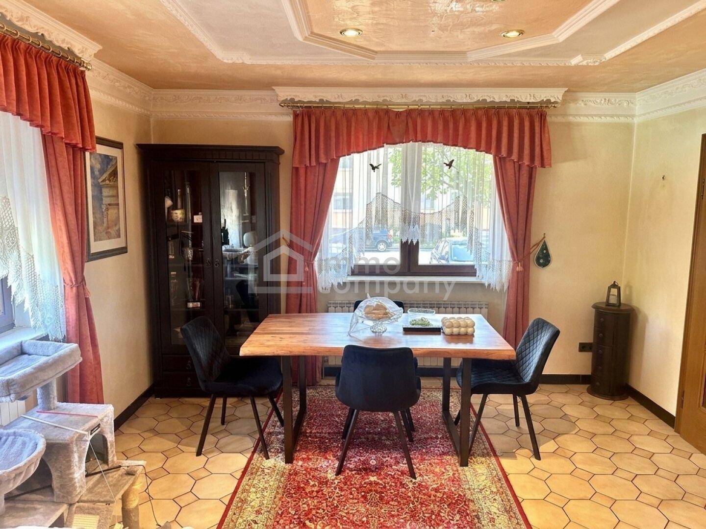 Essbereich mit Holztisch, dunklen Stühlen und traditioneller Dekoration, angrenzend an ein Fenster.