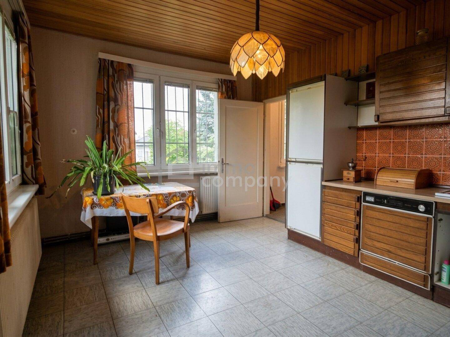 Traditionelle Küche mit Holzschränken, Fliesenboden und einem kleinen Essbereich am Fenster.