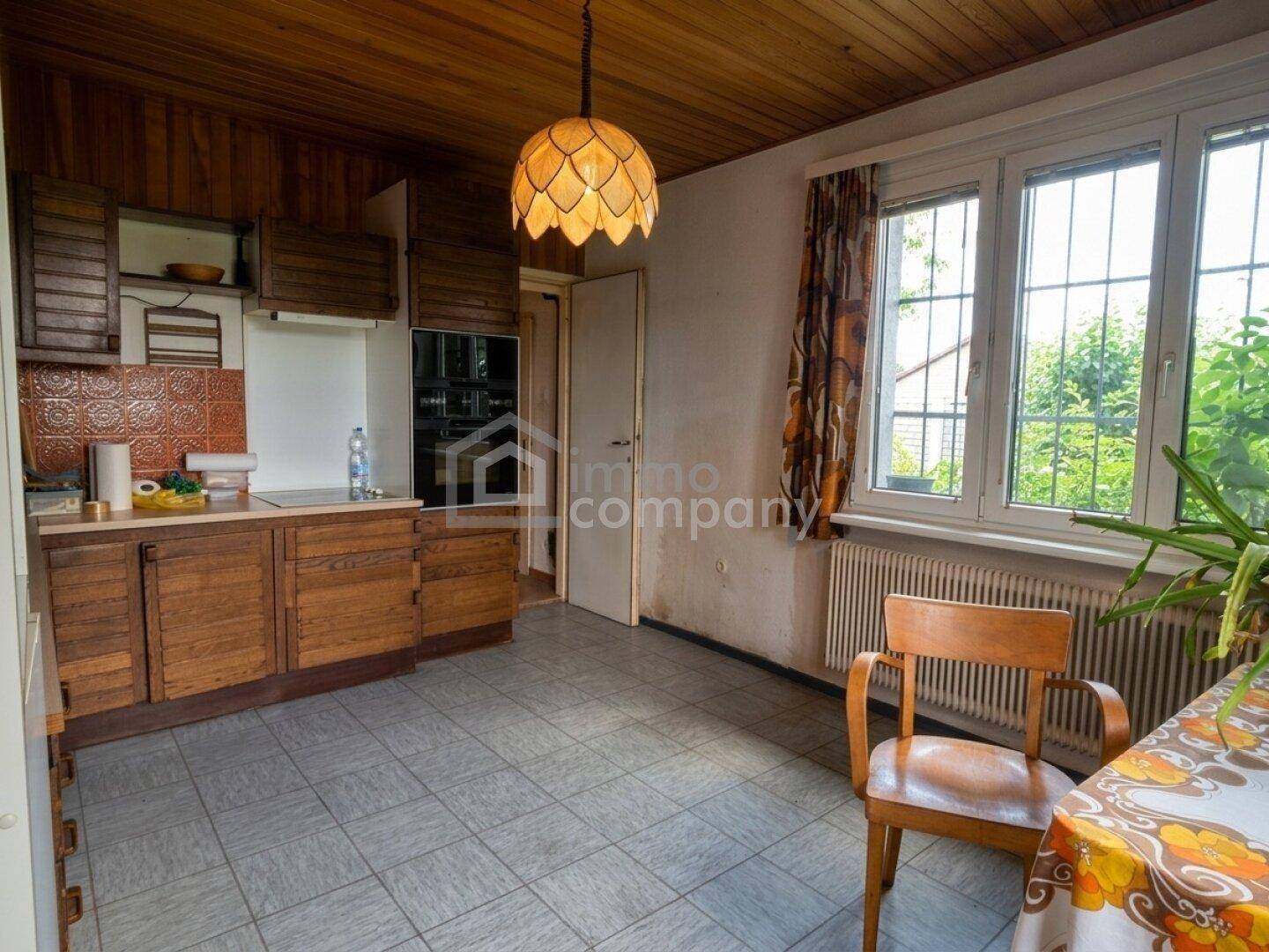 Gemütliche Küche im Landhausstil mit Holzvertäfelung, Fliesenboden und Blick ins Grüne.