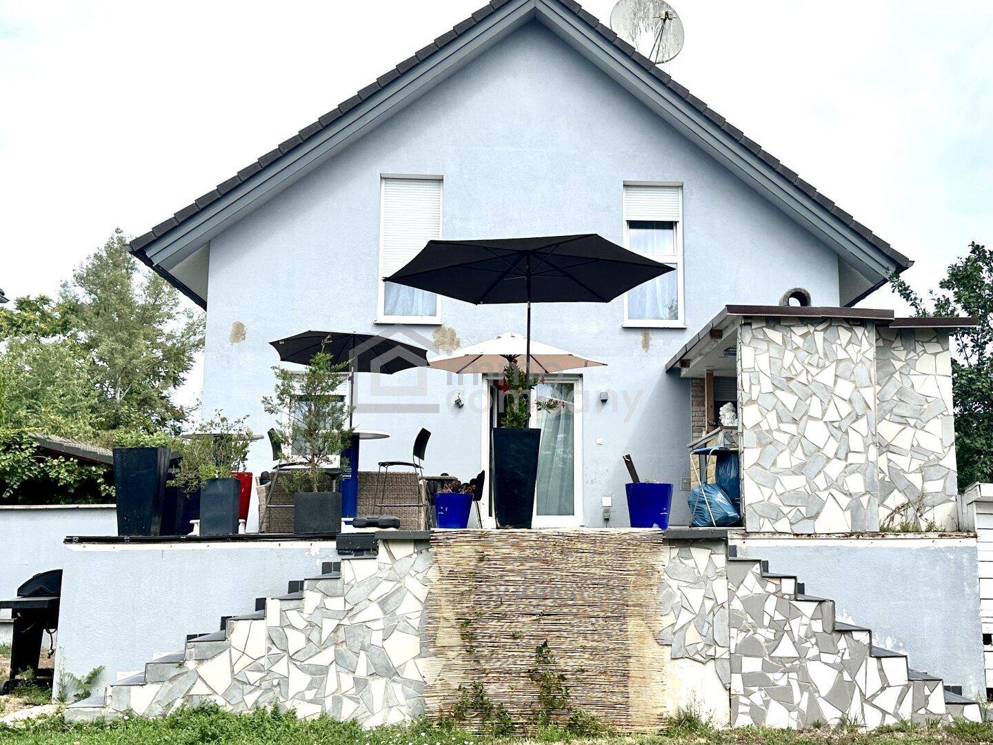 Rückseite des Hauses mit großer Terrasse, Außentreppe und Grillbereich.