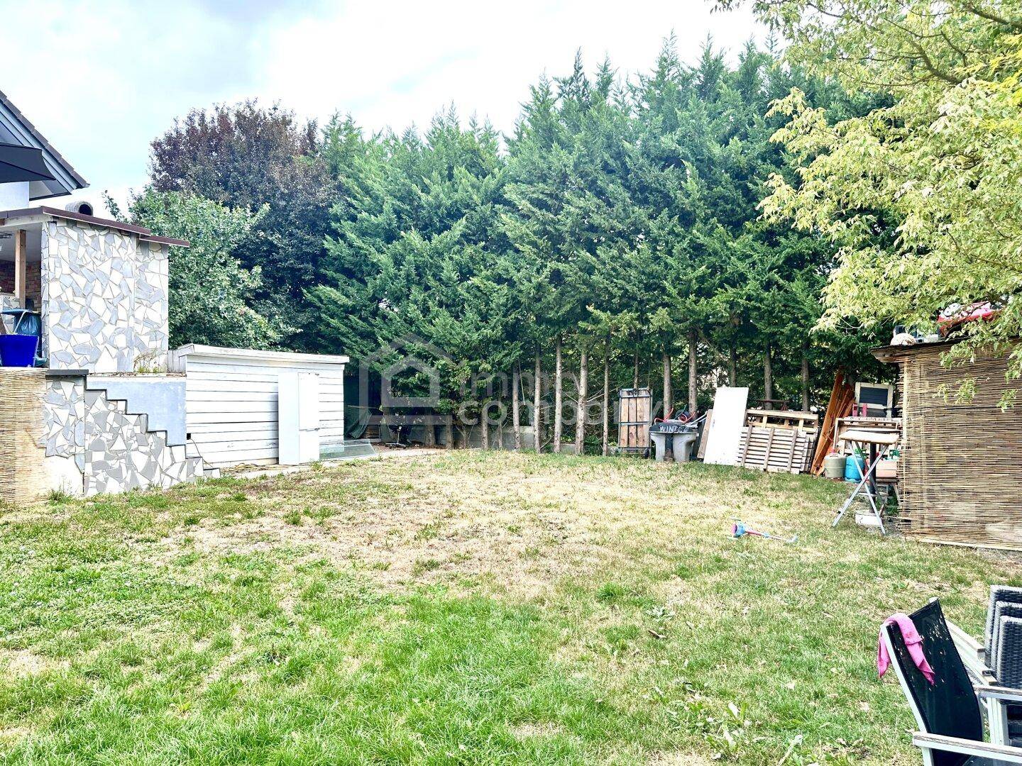 Großer Gartenbereich mit Rasenfläche, hohen Bäumen und Gartenhaus.