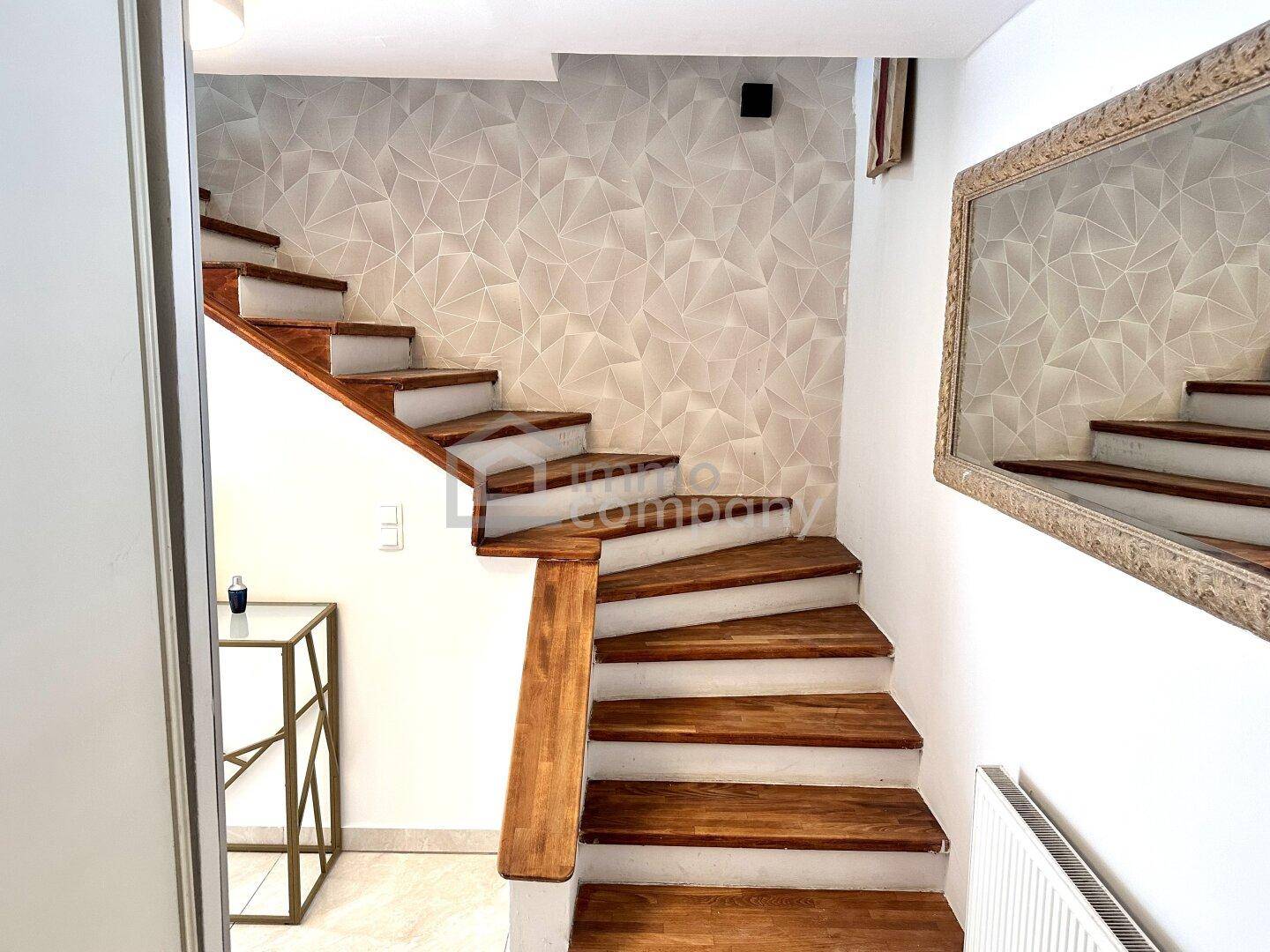 Heller Flur mit Holztreppe und dekorativer Wandgestaltung.