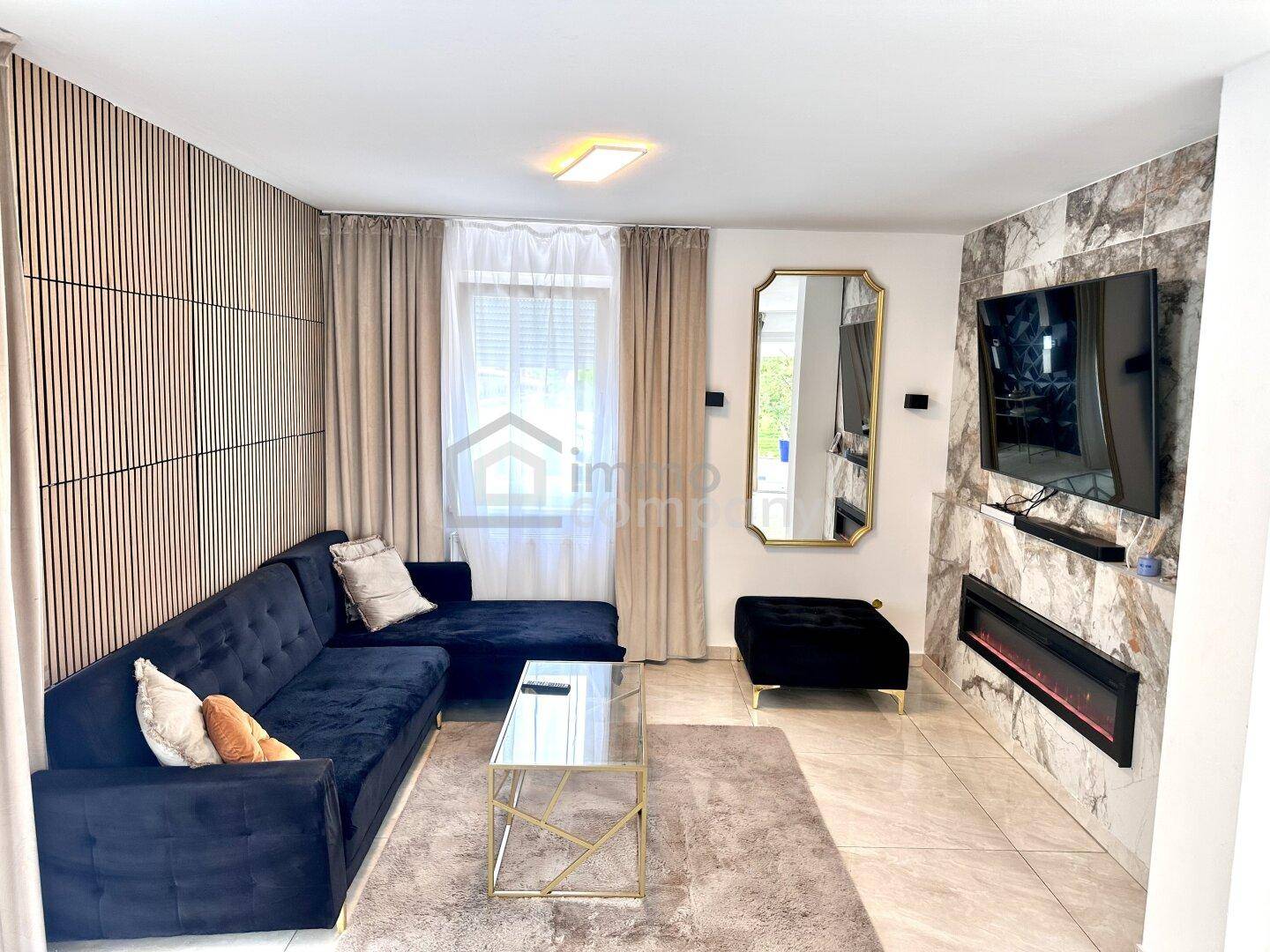 Modernes Wohnzimmer mit dunklem Sofa, Fliesenboden und dekorativer Wandverkleidung.
