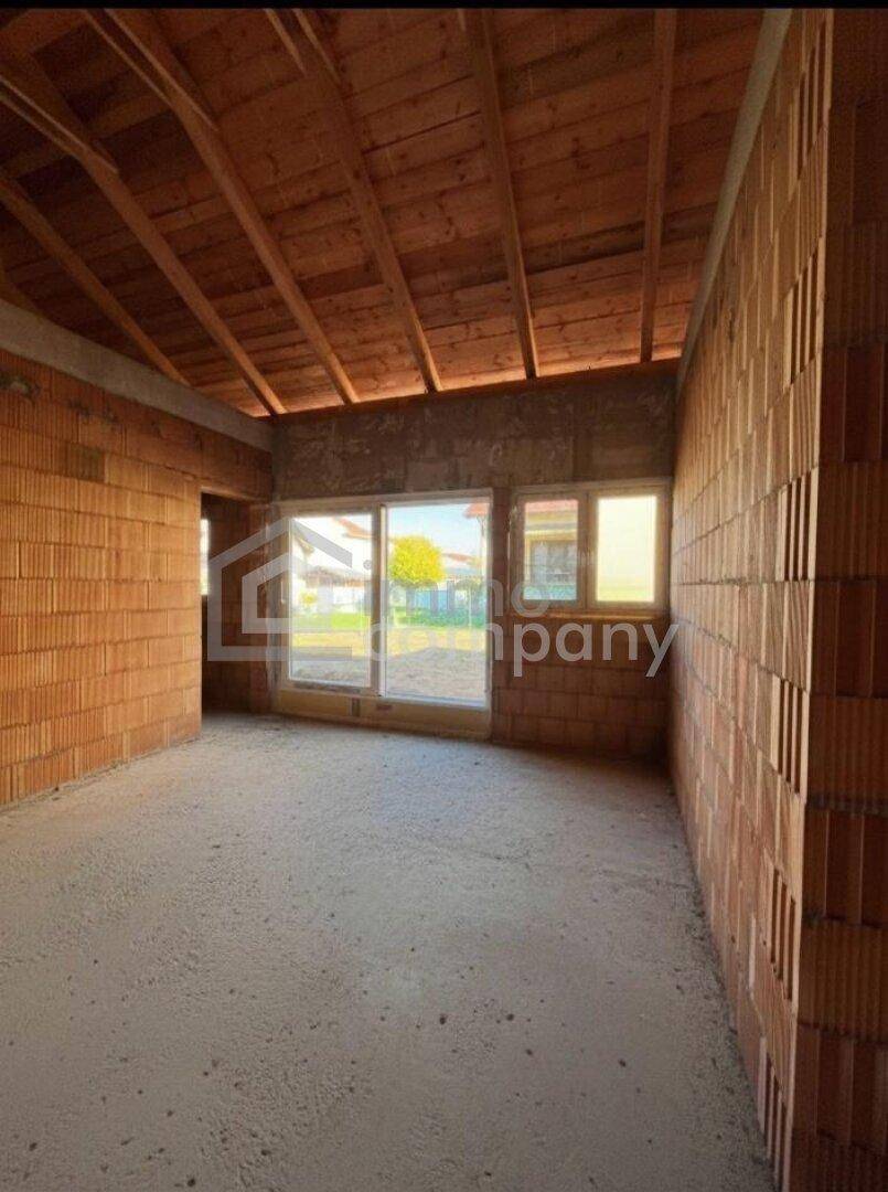 Innenraum im Rohbau mit sichtbaren Ziegelwänden und offener Holzkonstruktion des Daches.