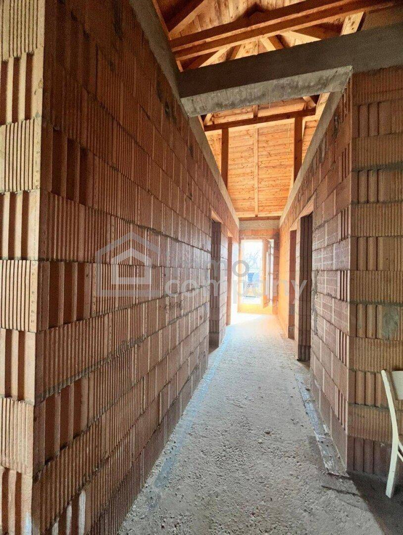Flur im Rohbau mit unverputzten Ziegelwänden und sichtbarer Holzkonstruktion des Daches.