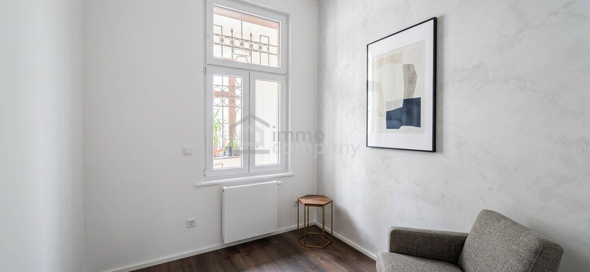 Gemütliche Ecke eines Zimmers mit Fenster, einem kleinen Beistelltisch und einem Sessel, ideal zum Entspannen.