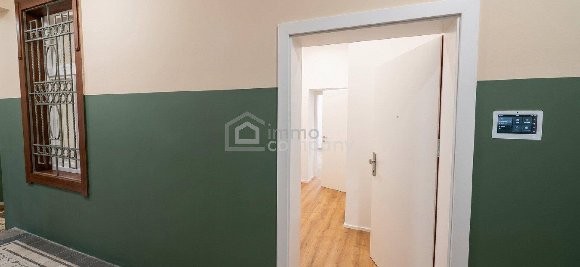 Flur mit zweifarbigen Wänden, einem Fenster mit Gitter und einem Smart-Home-Panel an der Wand.
