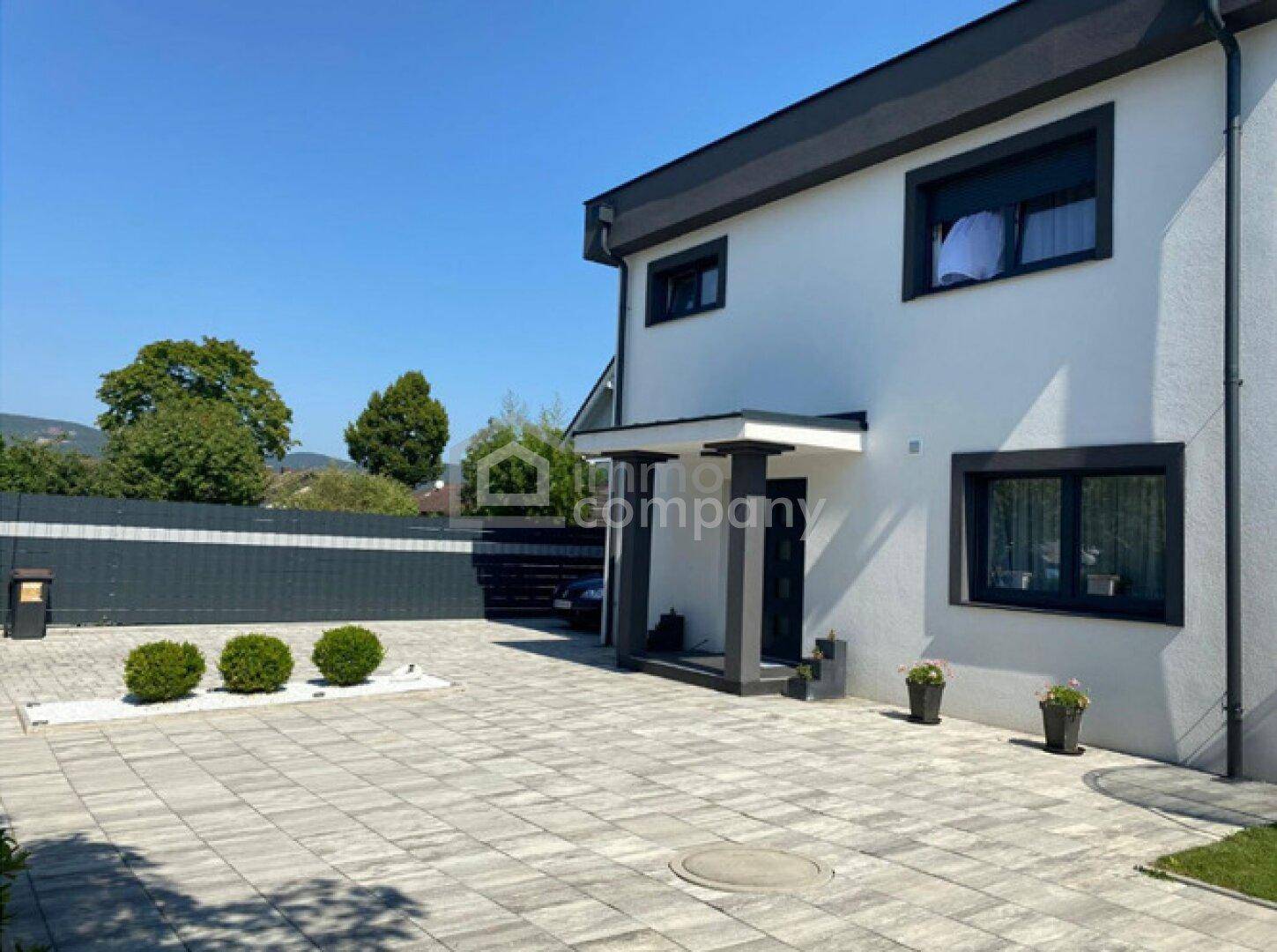 Moderne Hausfassade mit gepflasterter Auffahrt und gepflegten Sträuchern im Vorgarten.
