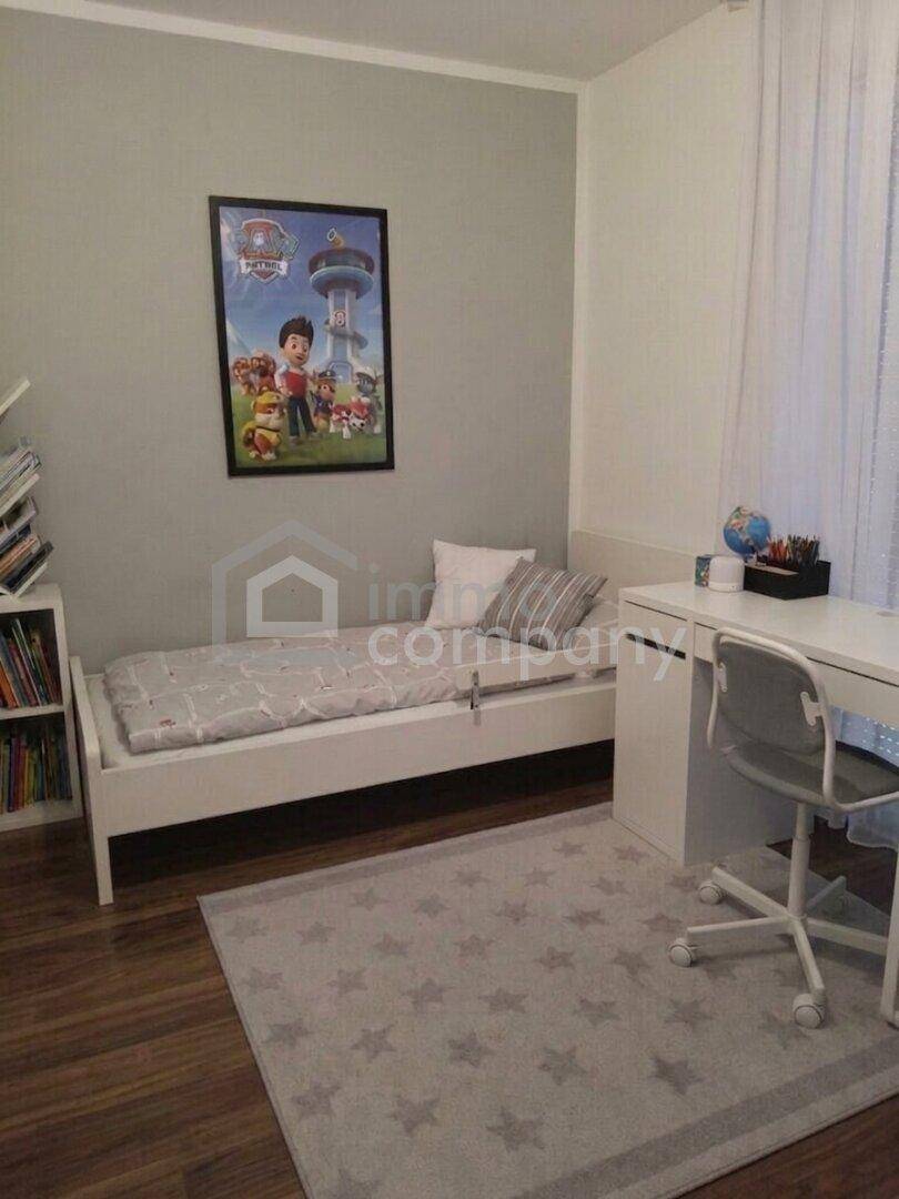Helles Kinderzimmer mit Einzelbett, Schreibtisch und einem Teppich mit Sternenmuster.
