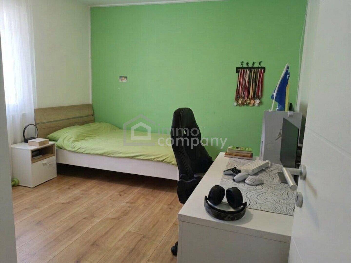Kinderzimmer mit grün gestrichener Wand, Holzboden und einem Einzelbett mit Schreibtisch.