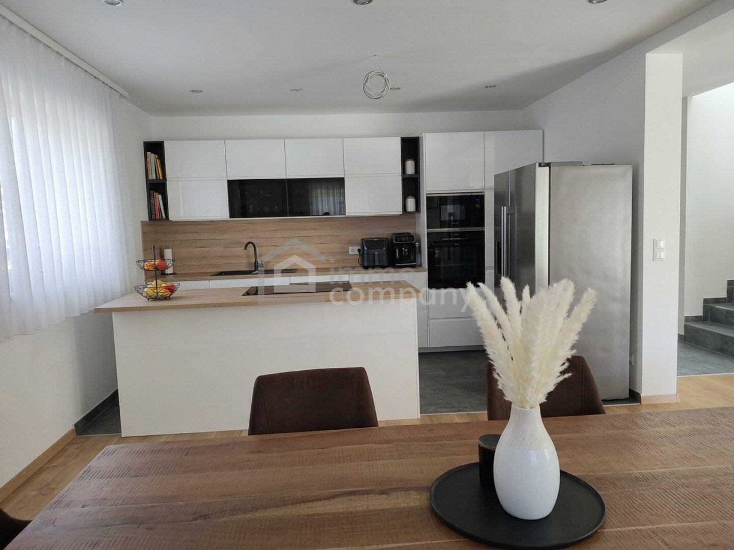 Moderne Küche mit weißer Front, Holztheke und integrierten Geräten, offen zum Essbereich.