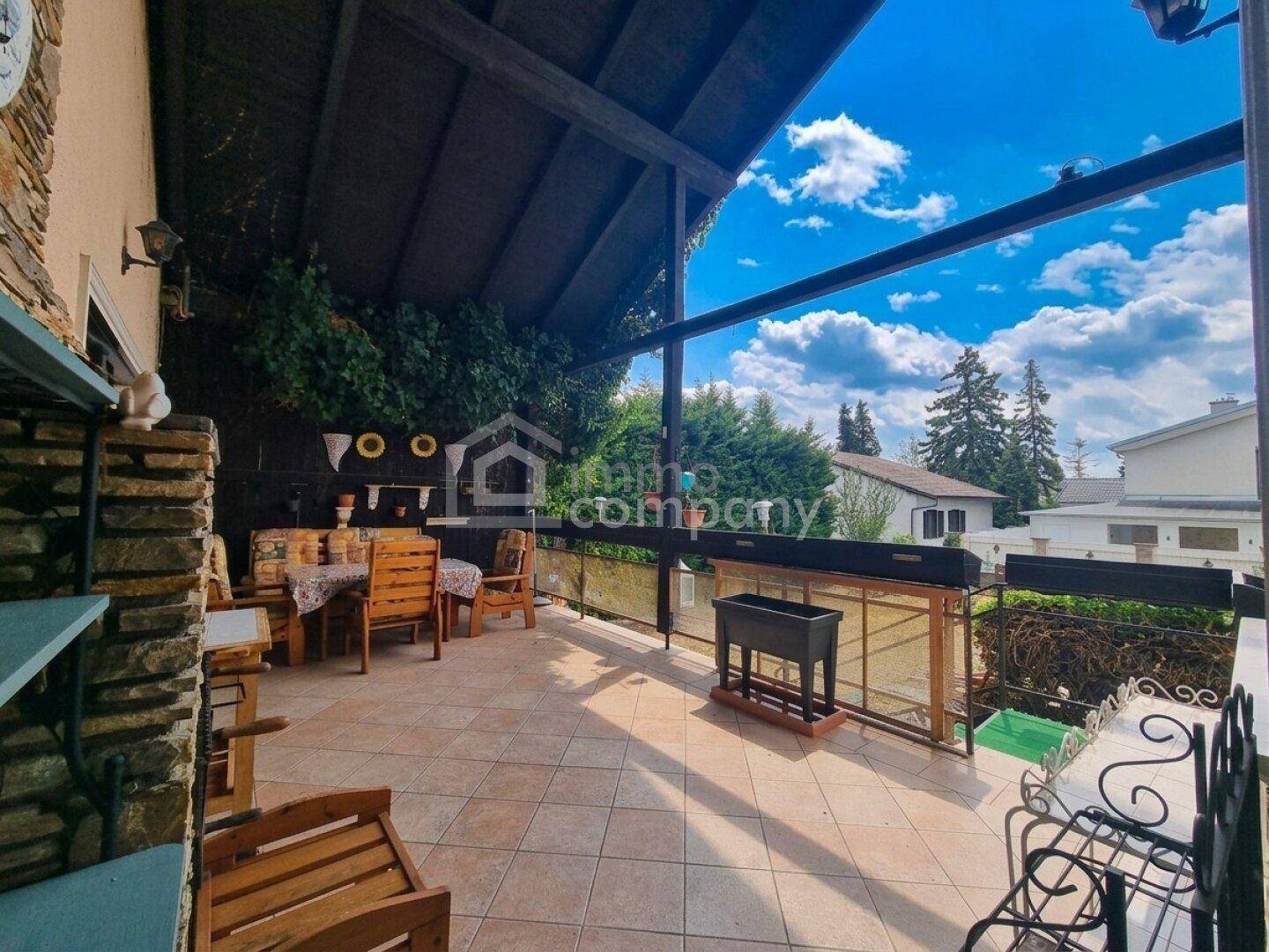 Überdachte Terrasse mit Fliesenboden und Holzmöbeln, ideal für entspannte Stunden im Freien.