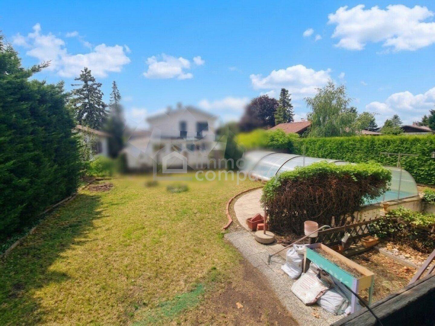 Gartenbereich mit Rasenfläche und einem überdachten Pool im Hintergrund unter blauem Himmel.