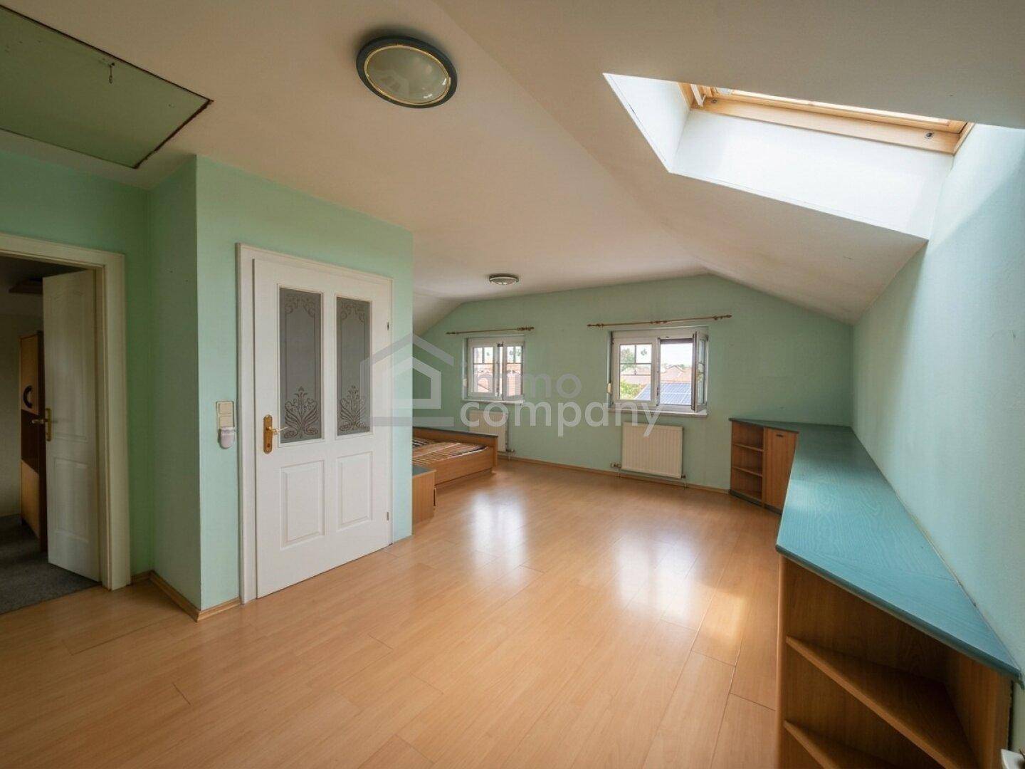 Dachzimmer mit schrägen Wänden, hellgrüner Farbgebung, Laminatboden und einem Dachfenster.