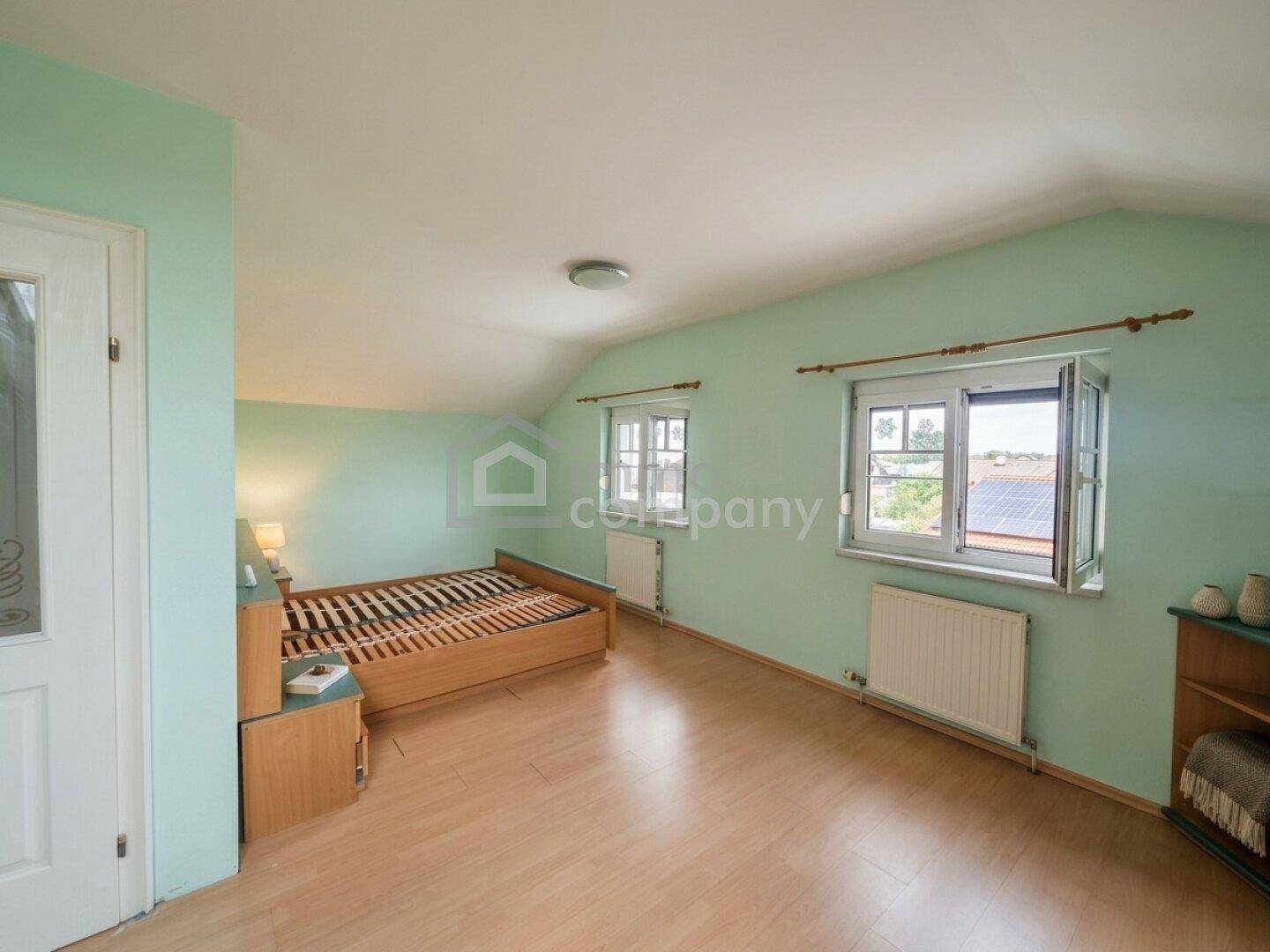Dachzimmer mit schrägen Wänden, Laminatboden und Blick aus dem Fenster auf die Umgebung.
