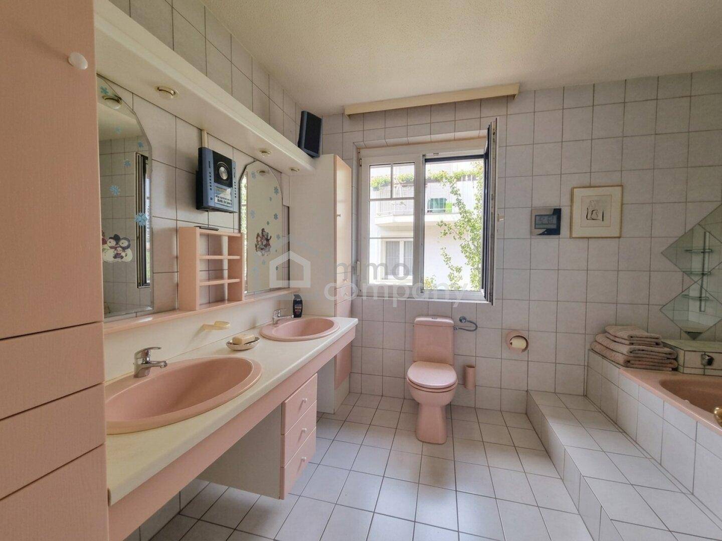 Badezimmer mit rosa Sanitärobjekten, weißen Fliesen und einem Fenster für Tageslicht.