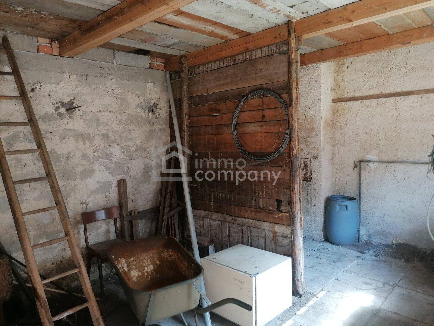 Rustikaler Abstellraum mit Holzbalken, rauen Wänden, einer Leiter und verschiedenen Geräten.
