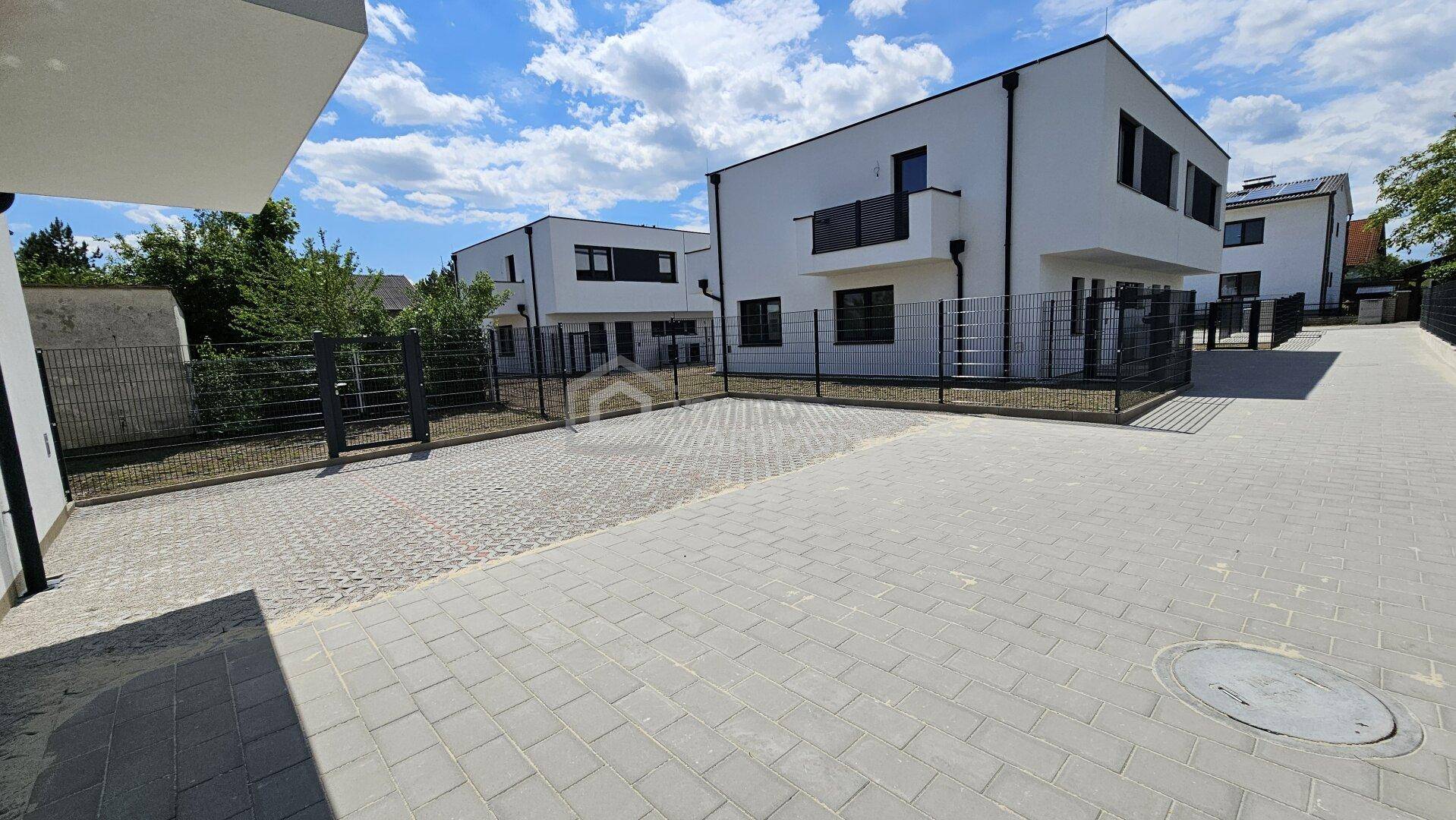 Außenansicht einer Reihe moderner Neubauten mit weißer Fassade und gepflasterten Wegen.