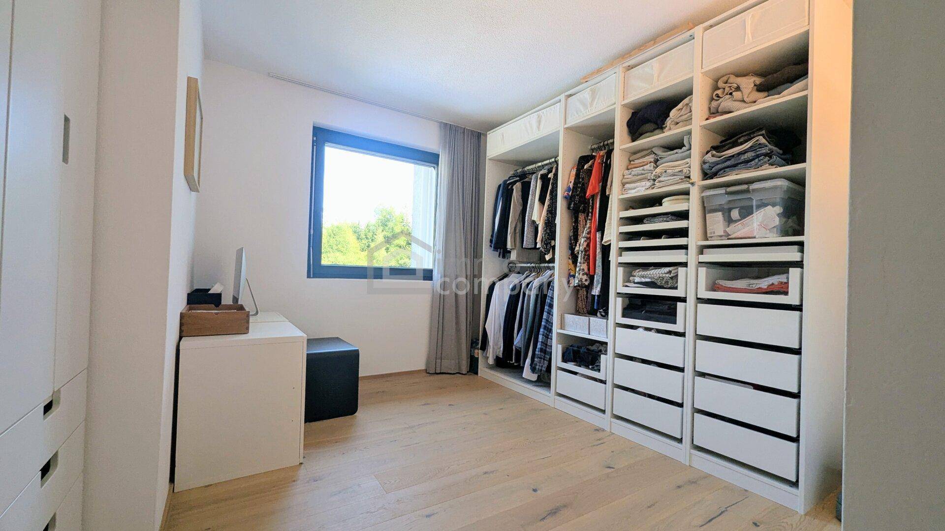 Geräumiger begehbarer Kleiderschrank mit viel Stauraum und Fenster, praktisch und gut organisiert.