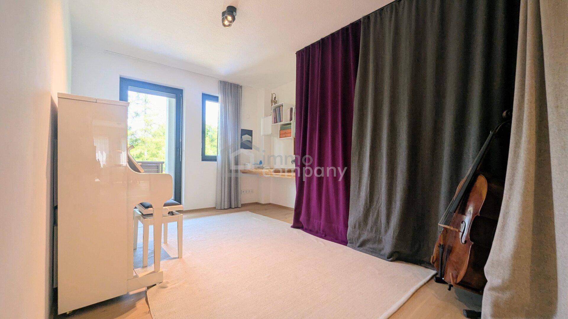 Helles Zimmer mit Klavier, Schreibtisch und Zugang zu einem Balkon, ideal für Musik oder Arbeit.
