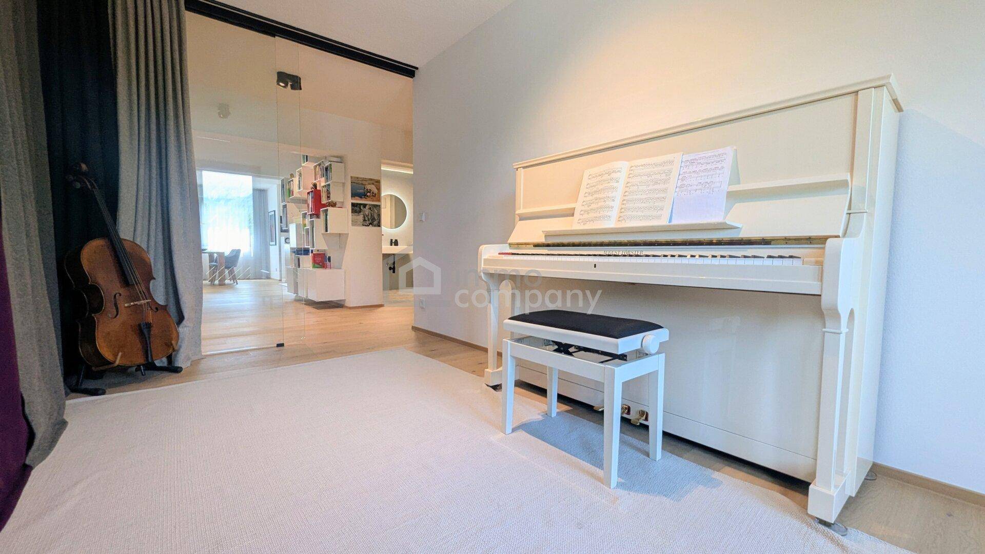Musikzimmer mit weißem Klavier und Blick in den offenen Wohnbereich, schafft eine inspirierende Atmosphäre.
