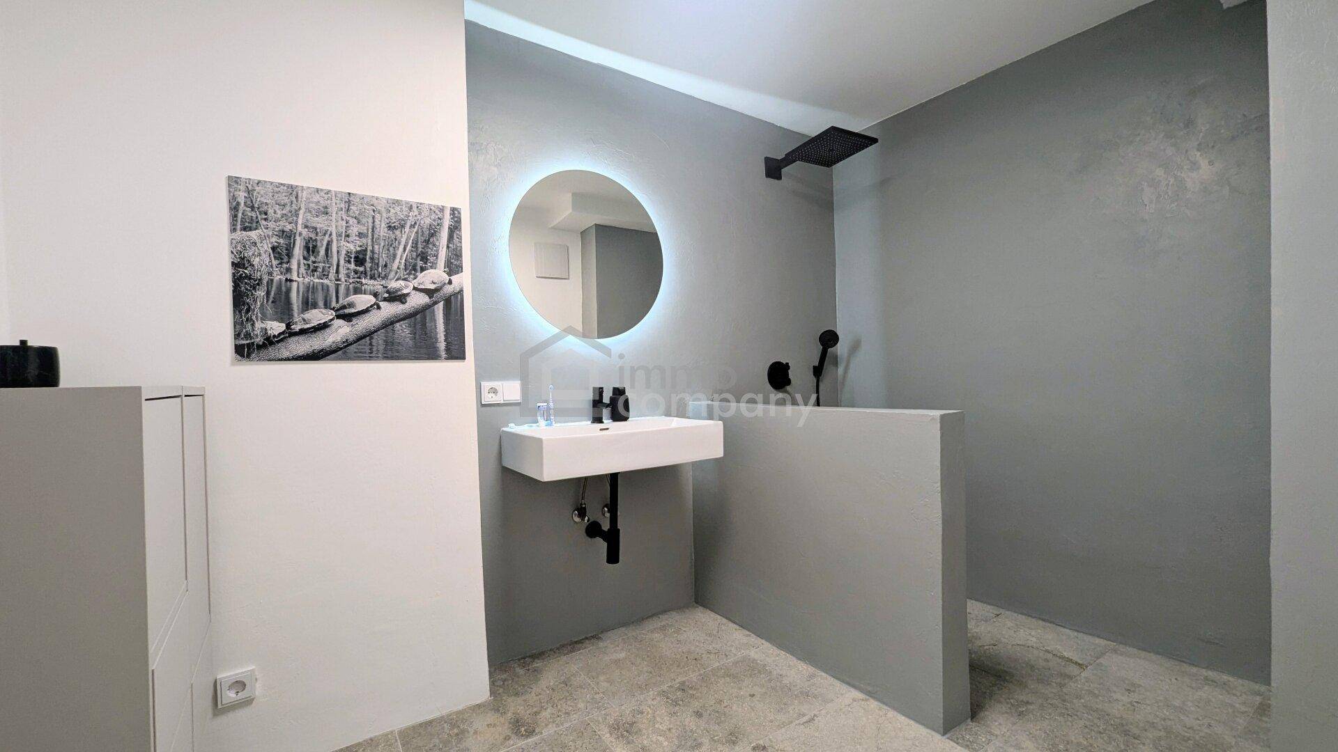 Modernes Badezimmer mit schwebendem Waschbecken, beleuchtetem Spiegel und begehbarer Dusche.