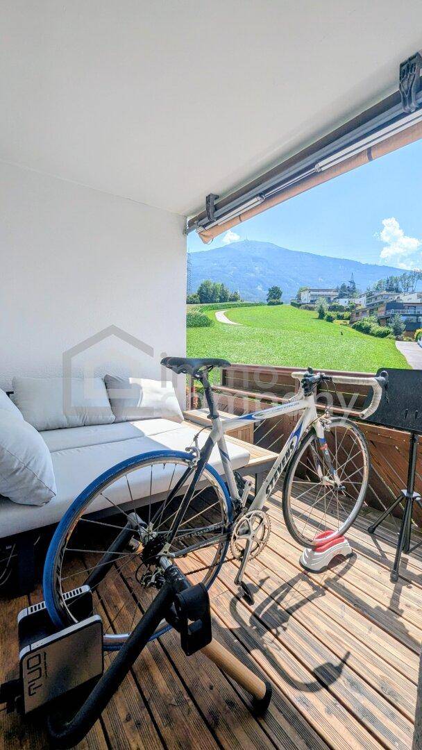 Sonniger Balkon mit Holzboden, Sitzgelegenheiten und weitem Blick auf die Berge und grüne Landschaft.