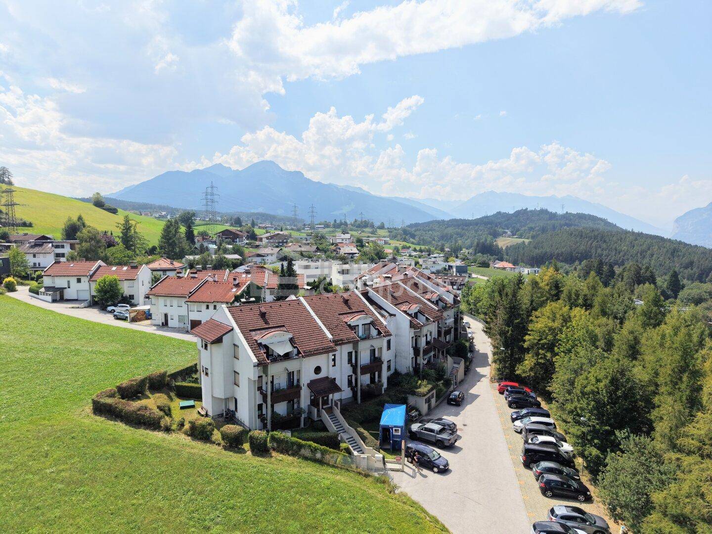 Reihenhaussiedlung in ländlicher Umgebung mit vielen Parkplätzen und weitem Bergblick.
