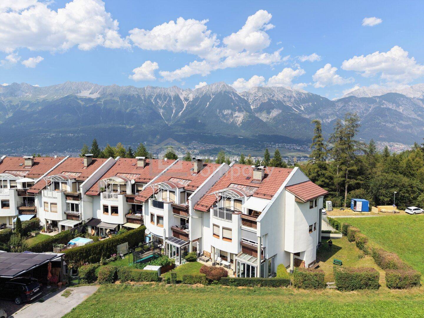 Reihenhäuser in einer grünen Umgebung mit beeindruckendem Bergblick unter blauem Himmel.