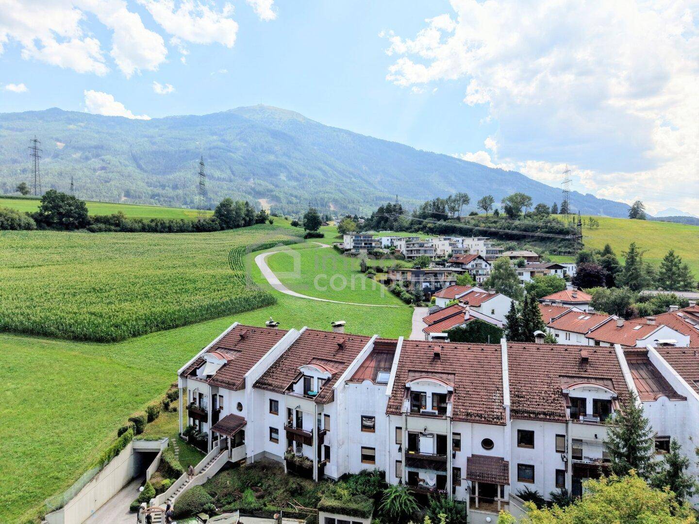 Reihenhäuser eingebettet in eine weite grüne Landschaft mit Feldern und Bergen im Hintergrund.