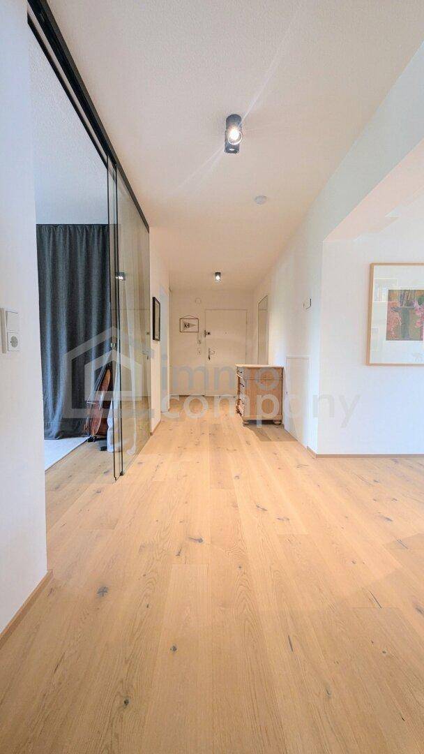 Langer Flur mit Holzboden und einer modernen Glasschiebetür, die Licht hereinlässt.