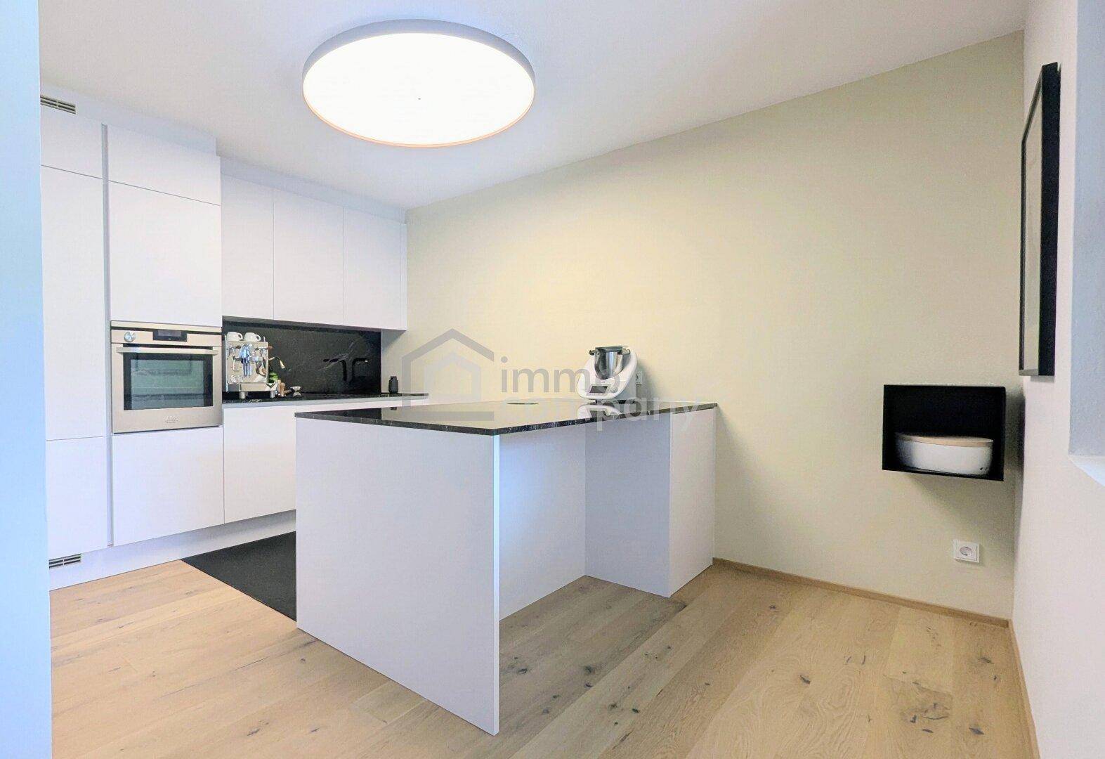 Helle, moderne Küche mit Kochinsel, weißen Fronten und Holzboden, perfekt für kulinarische Erlebnisse.